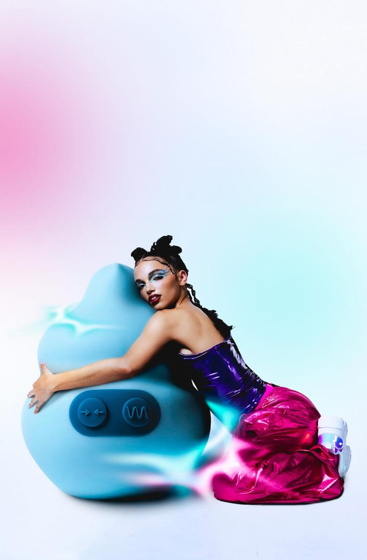 Model dressed in a metallic purple tube top, metallic bright pink pants, and white sneakers hugging a light blue life-sized Squish vibrator with a pink and blue gradient background