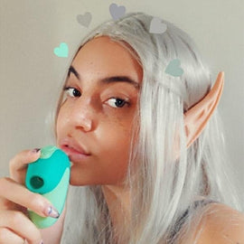 Model wearing silver wig and elf ears holding the Unbound Puff Product Suction Toy in mint green