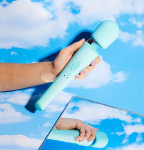 photo of hand holding an ollie aqua wand vibrator over a mirror on a cloud background